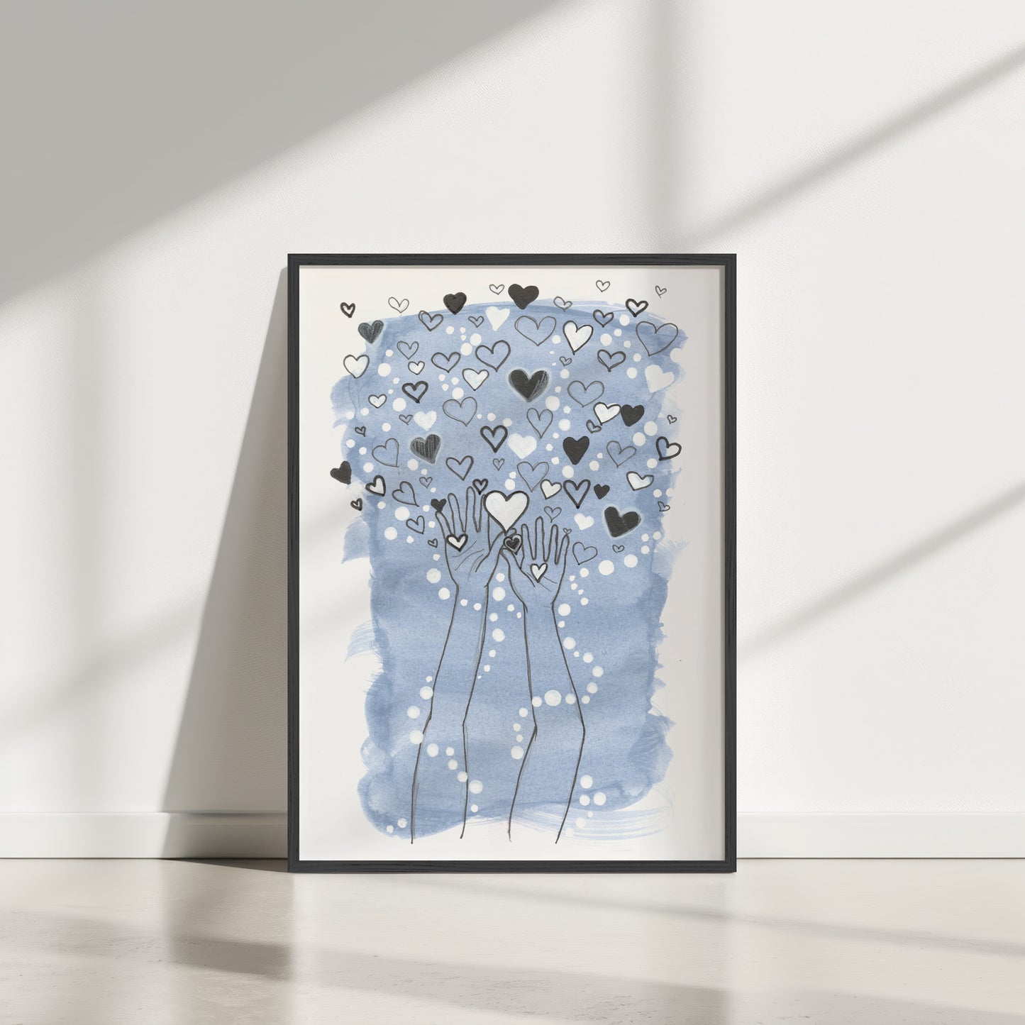 Framed artwork with hands holding hearts against a blue watercolor background on a white wall.