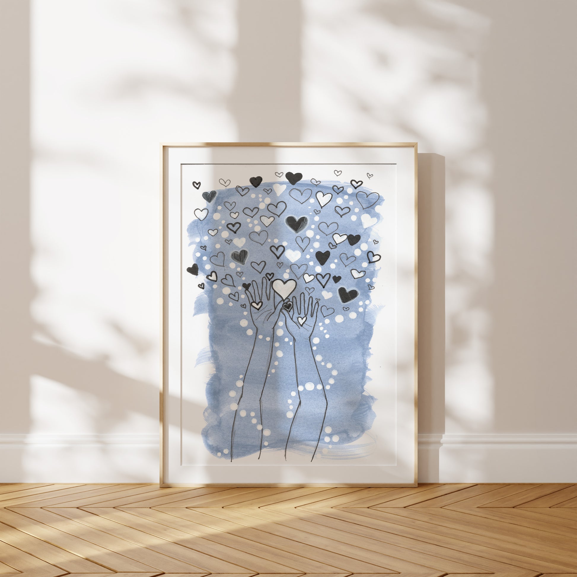 Framed artwork with hands holding hearts against a light blue background on a wooden floor.