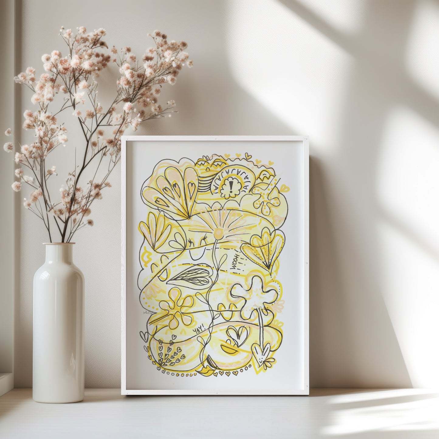 Framed yellow floral artwork on a white surface with a vase of dried flowers.